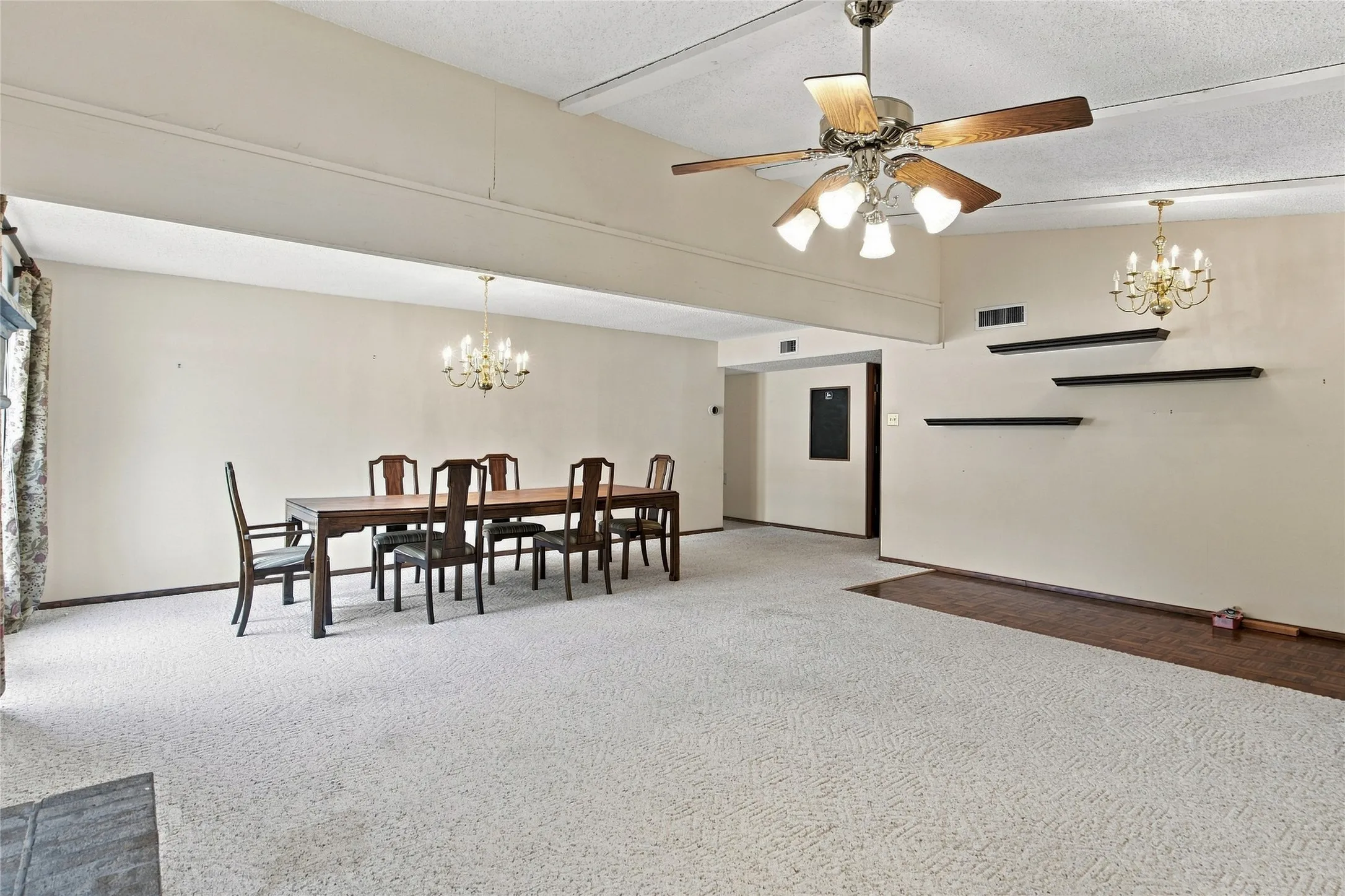 Spacious room featuring vaulted ceilings, a ceiling fan with integrated lighting, recessed wall shelves, and a brass chandelier