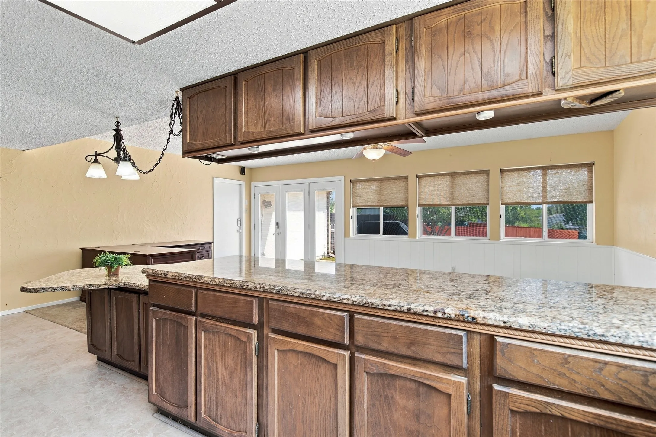 Kitchen featuring extensive wood cabinetry, granite countertops, a built-in breakfast bar, recessed lighting, and multiple windows with blinds