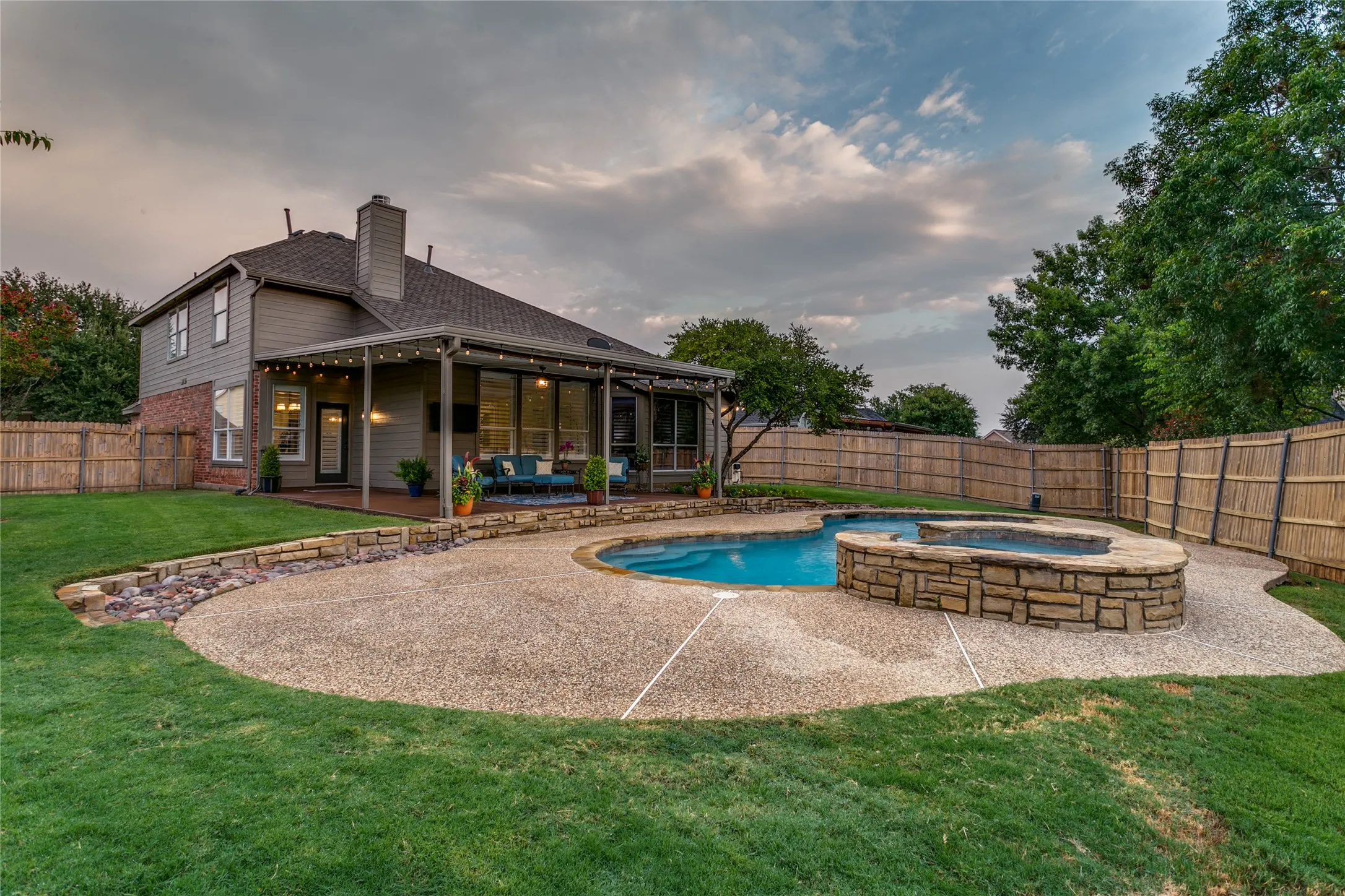 Expansive backyard featuring a curved concrete patio, in-ground swimming pool, and stone spa