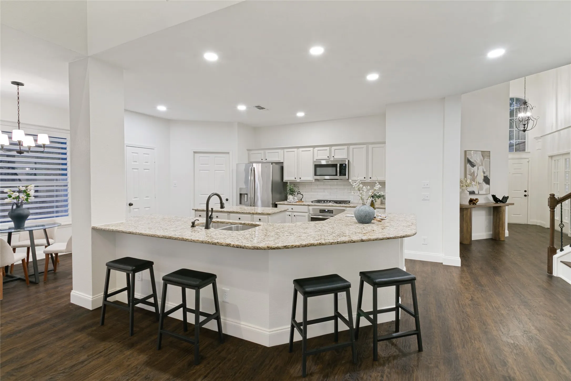 Open-concept kitchen featuring an expansive island with a built-in sink, stainless steel appliances, white cabinetry, and recessed lighting