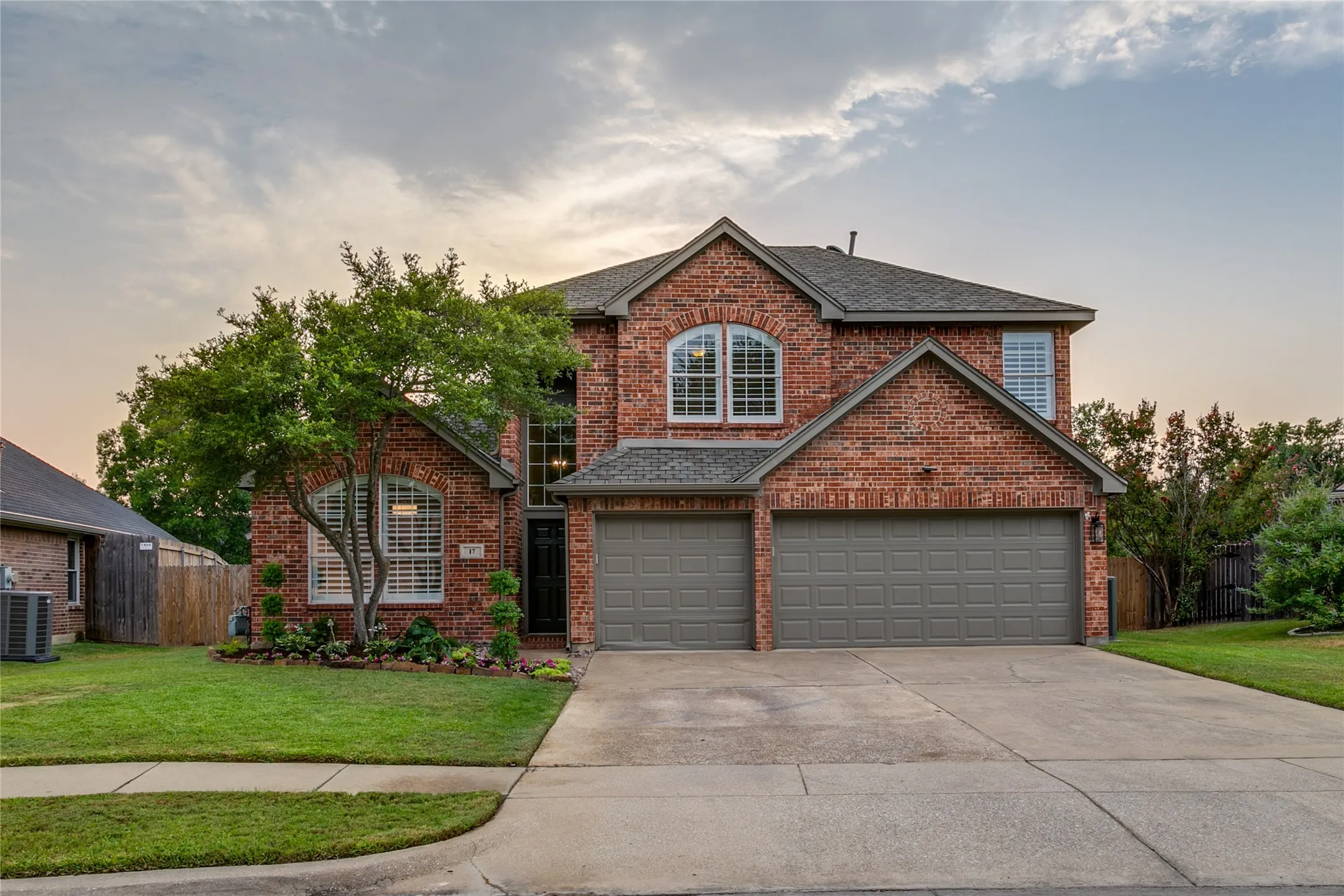 Traditional brick exterior with an attached three-car garage, freshly installed landscaping, and an arched window detail.