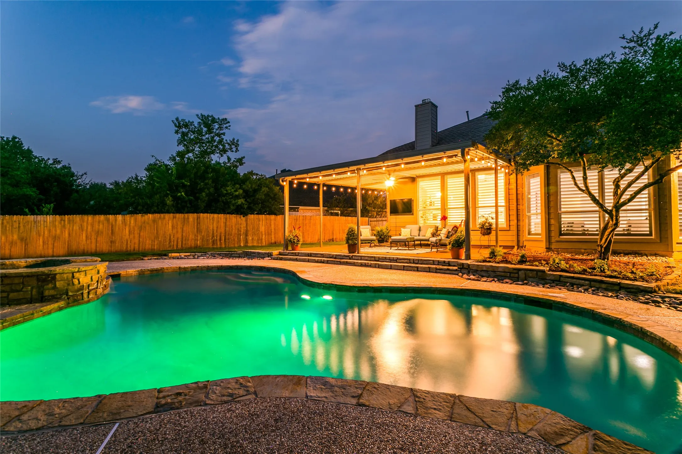 Curved swimming pool with integrated spa, stone coping, and illuminated water