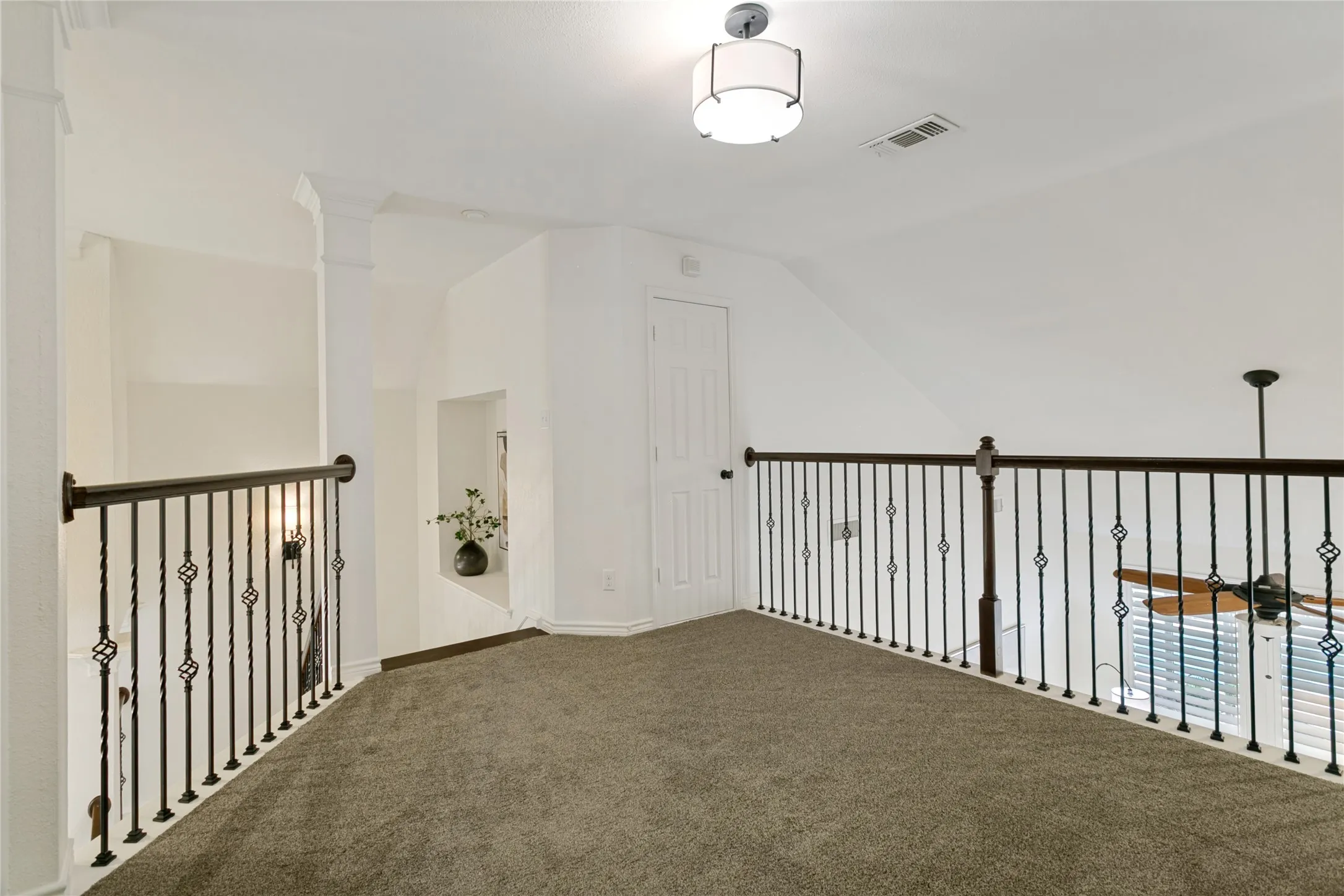 Carpeted loft area featuring wrought iron railings, a built-in display nook, a flush mount light fixture, and a ceiling fan