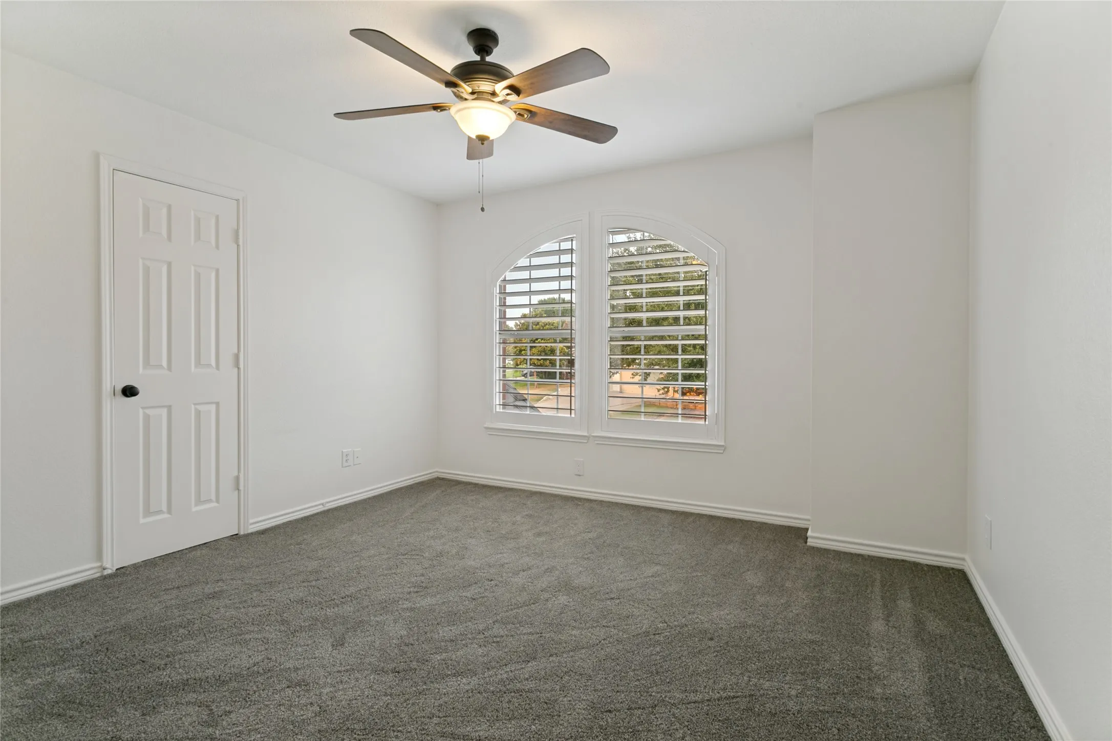 Arched window with plantation shutters, ceiling fan with integrated lighting, paneled door, and neutral carpet flooring