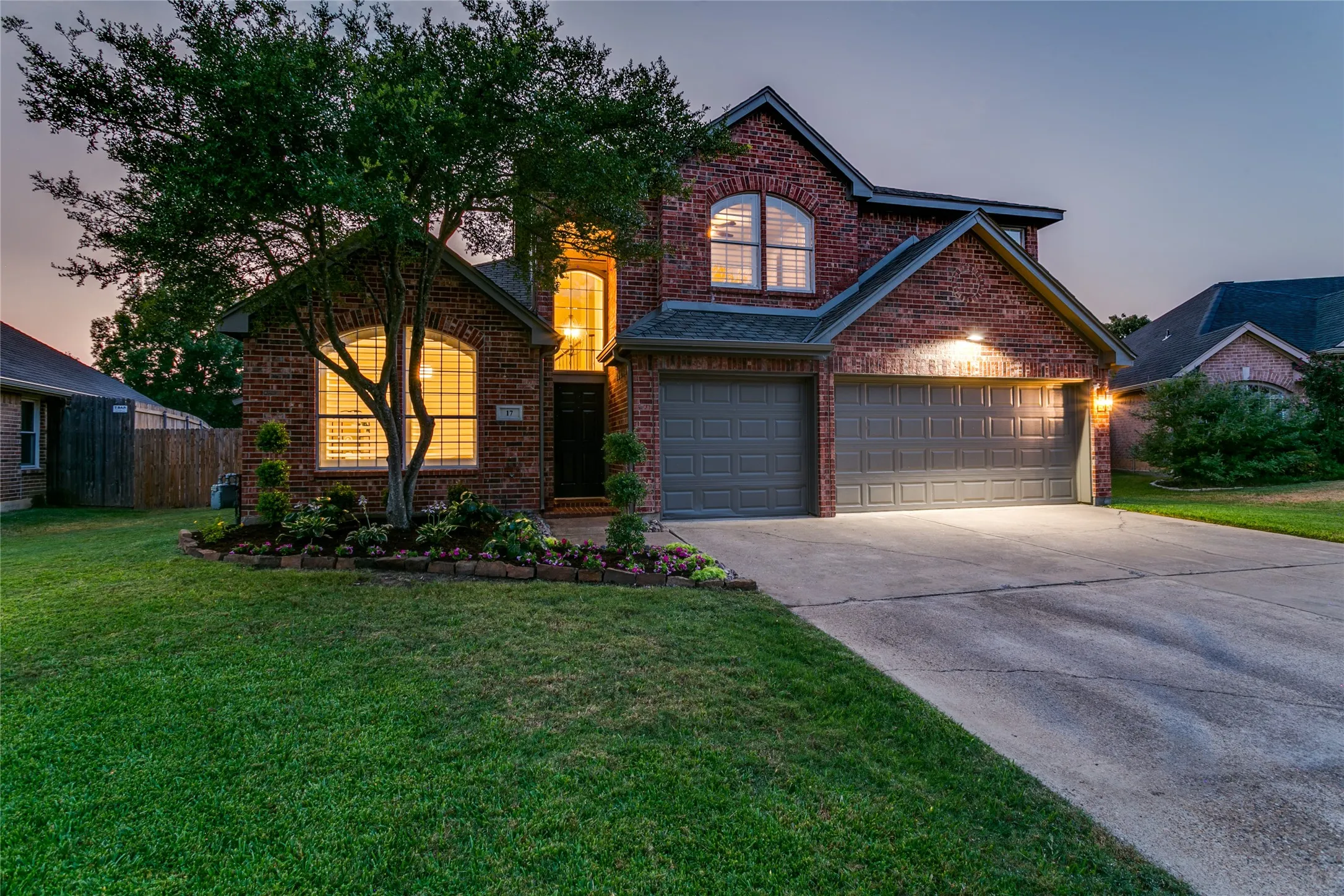 Brick exterior with arched windows, attached three-car garage, concrete driveway, and established landscaping