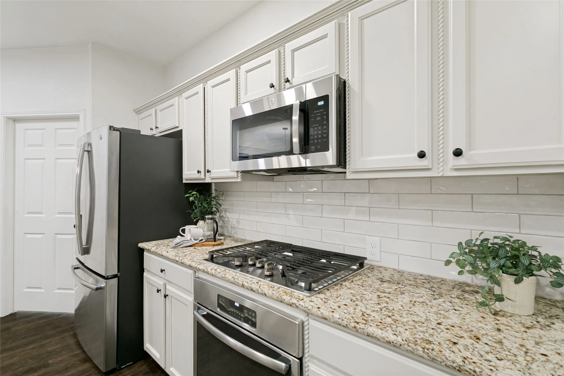 White cabinetry with rope trim accents, stainless steel appliances, speckled stone countertops, and a white pearl finish subway tile backsplash