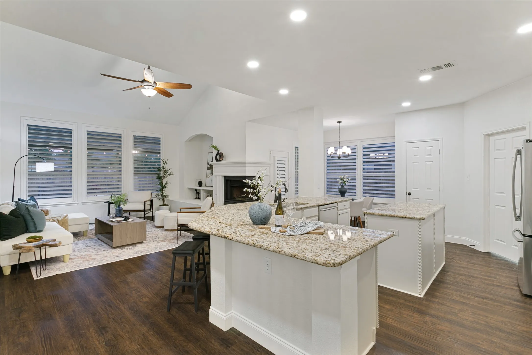 Vaulted ceiling with ceiling fan, recessed lighting, wood-finish flooring, white plantation shutters, and a fireplace with a white mantel