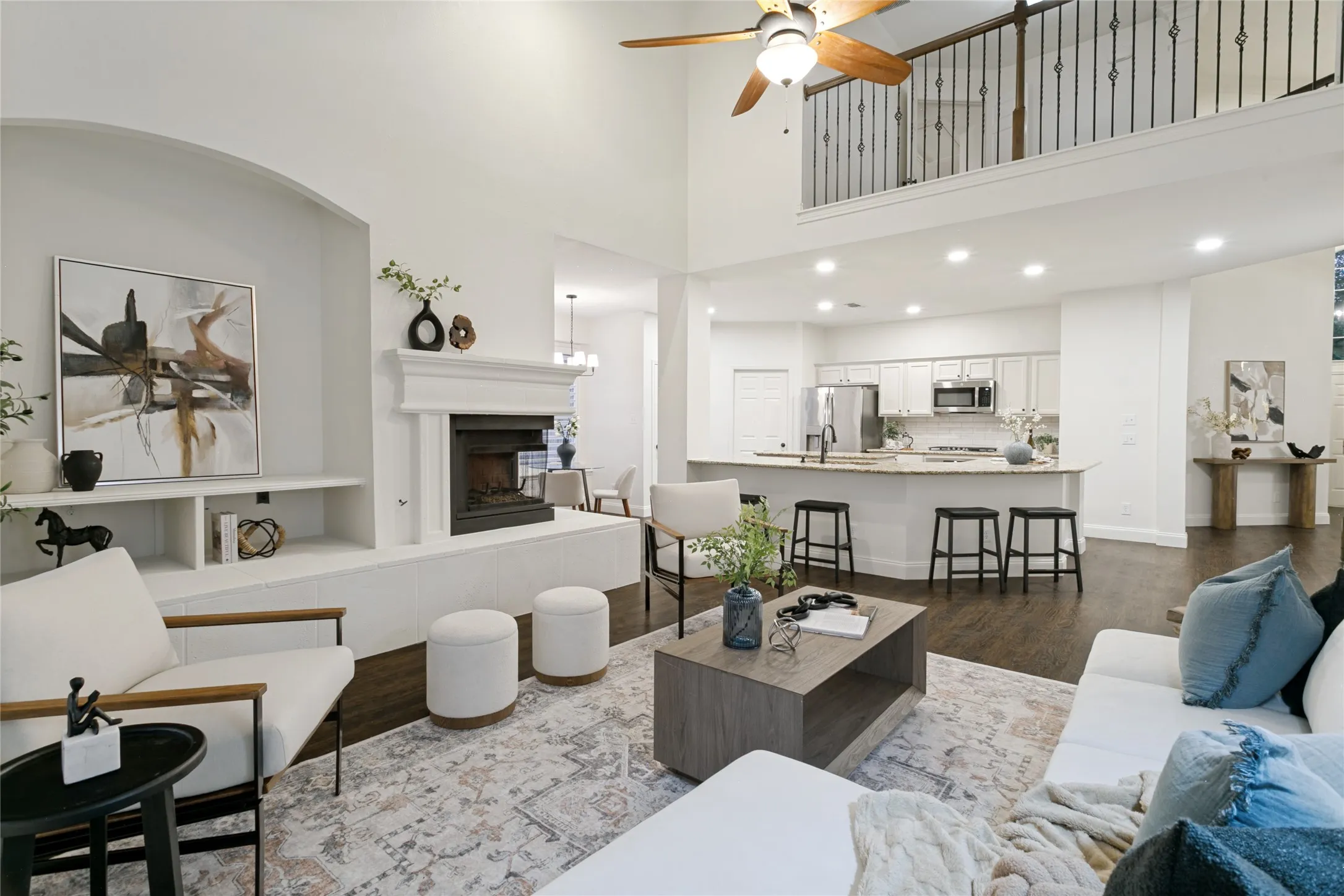 Soaring ceilings, a built-in fireplace, dark wood-finish flooring, a kitchen island with seating, and a second-story interior loft overlooking both the front foyer and open concept living features  wrought iron railing