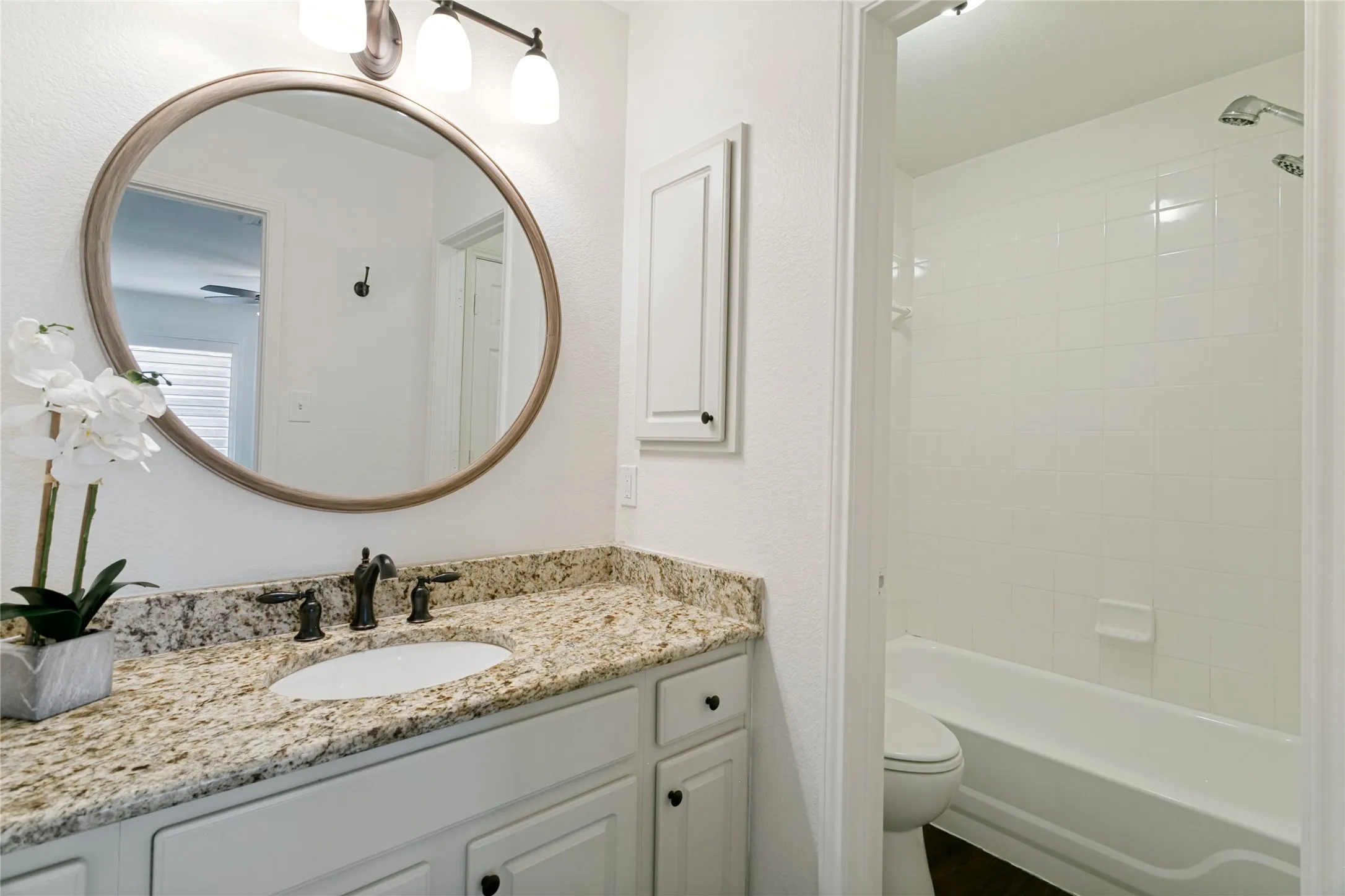 Bathroom featuring a vanity with a light-toned countertop, a dark-toned faucet, and a round framed mirror