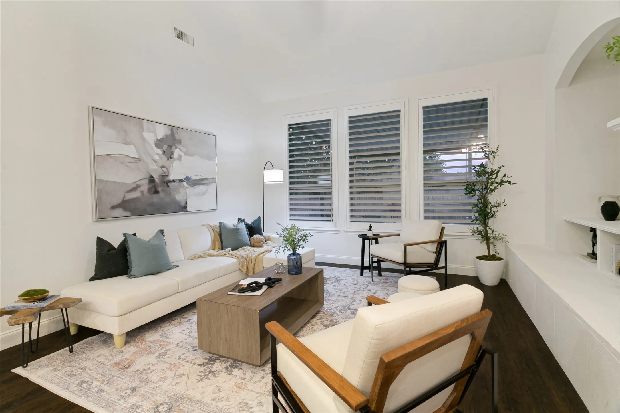 Vaulted ceiling, dark wood-finish flooring, white walls, multiple windows with shutters, and a built-in arched alcove