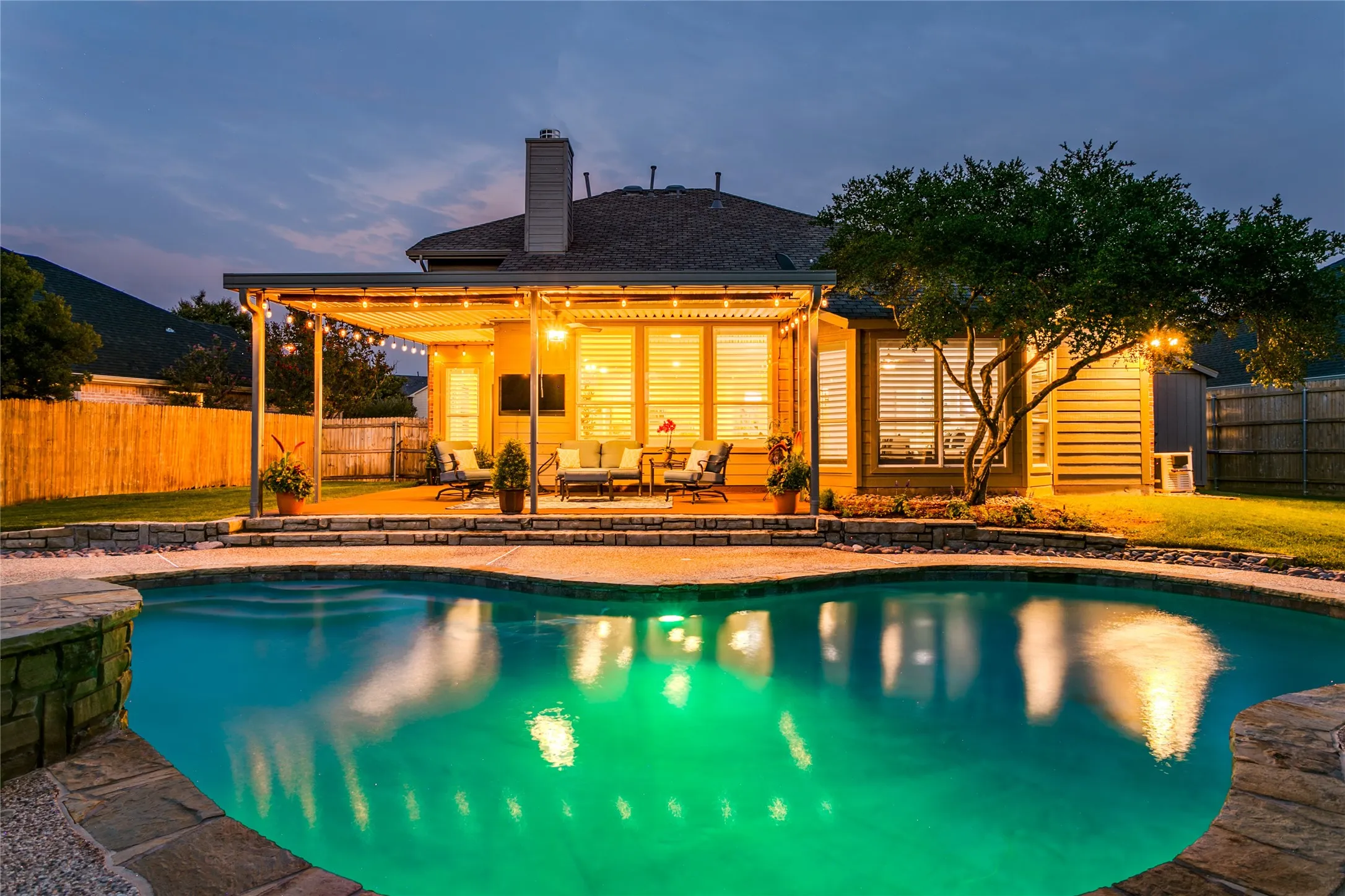 Resort-style backyard featuring a oversized custom-shaped swimming pool with stone coping, a spacious covered patio, and a manicured lawn