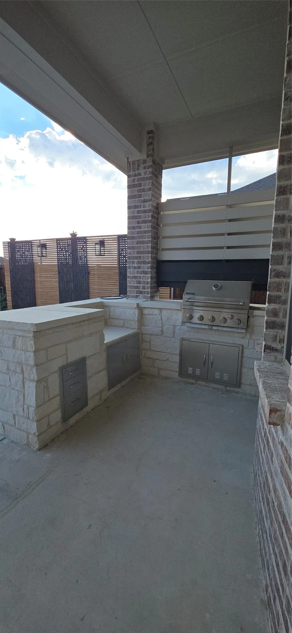 Covered outdoor patio featuring a built-in stone grill station, integrated stainless steel barbecue, stone countertop, and concrete flooring