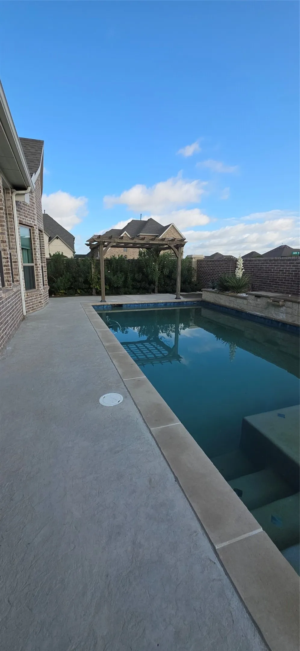 Spacious concrete patio with an adjacent rectangular swimming pool, featuring a stone coping and integrated steps