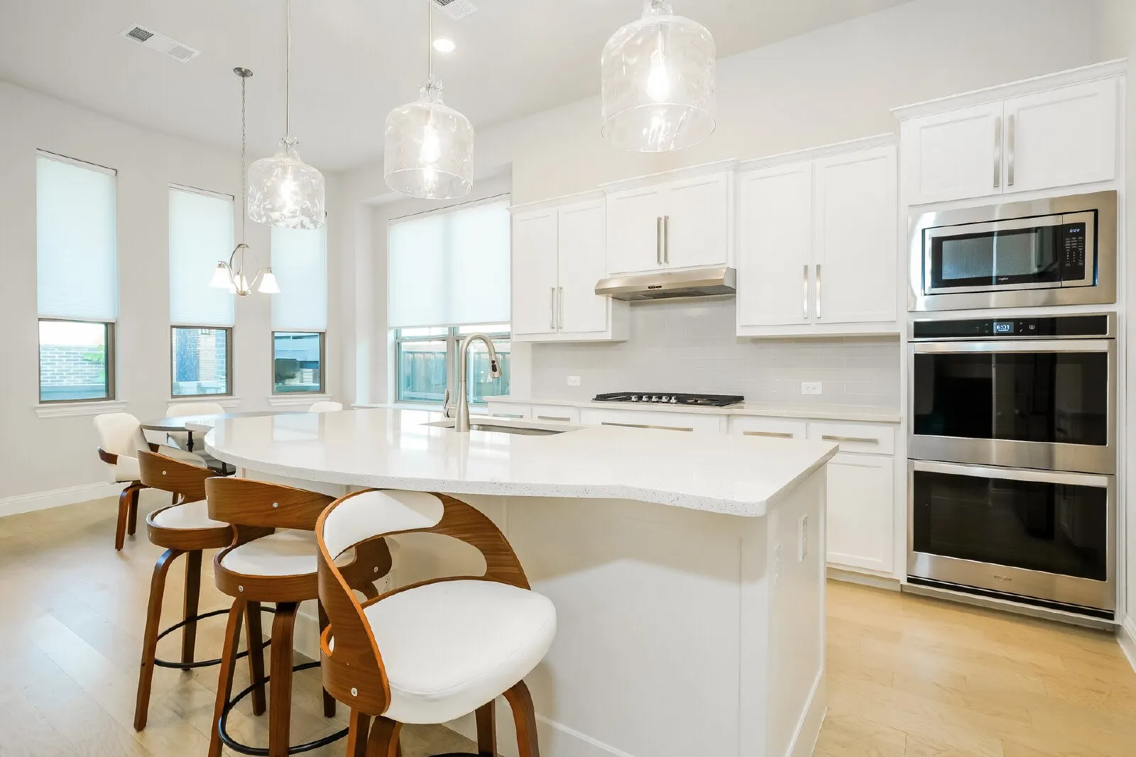 Light wood-finish flooring, white cabinetry, integrated stainless steel appliances, large kitchen island with counter seating, and pendant lighting