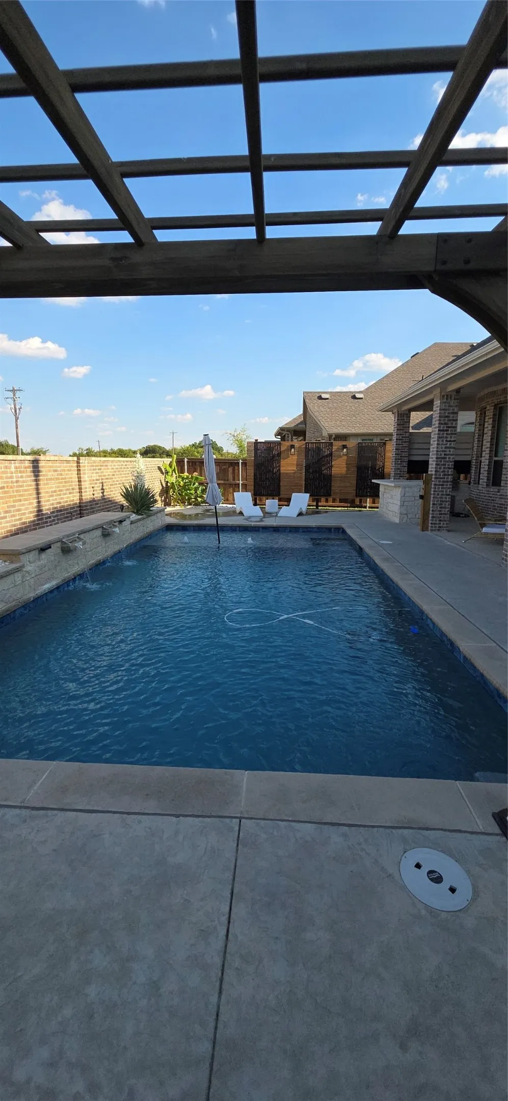 Expansive outdoor living area featuring a rectangular swimming pool, integrated water features, and a wood pergola