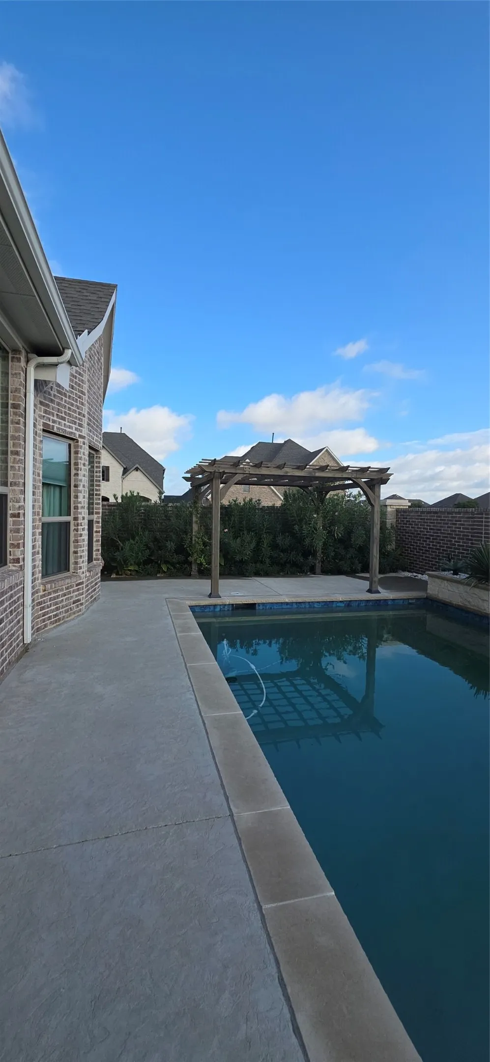 Brick exterior, in-ground swimming pool, concrete patio, wooden pergola, and privacy landscaping