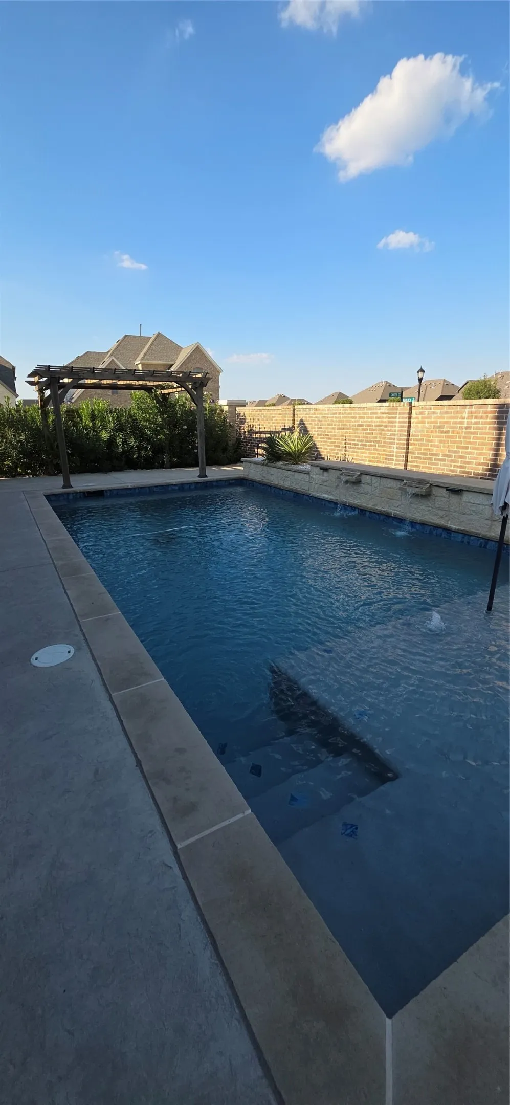In-ground swimming pool with integrated steps, concrete patio surround, and a coordinating stone accent wall with water features
