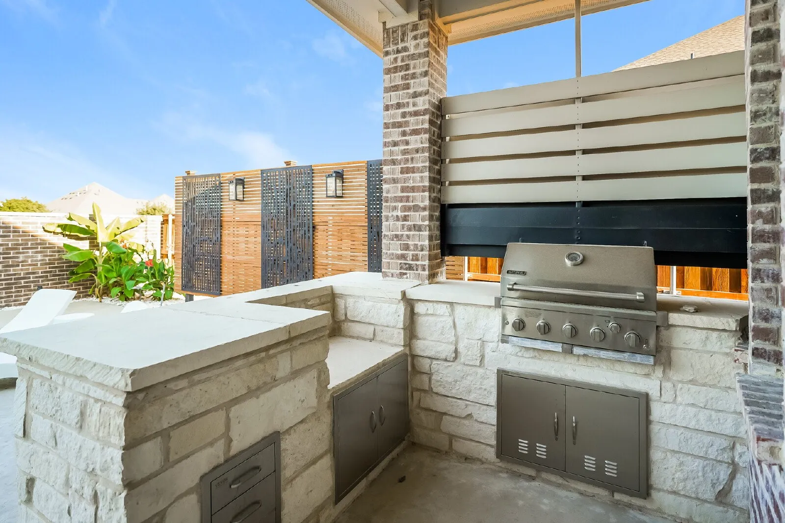 Outdoor kitchen featuring a built-in stainless steel grill, stone veneer base, and integrated storage