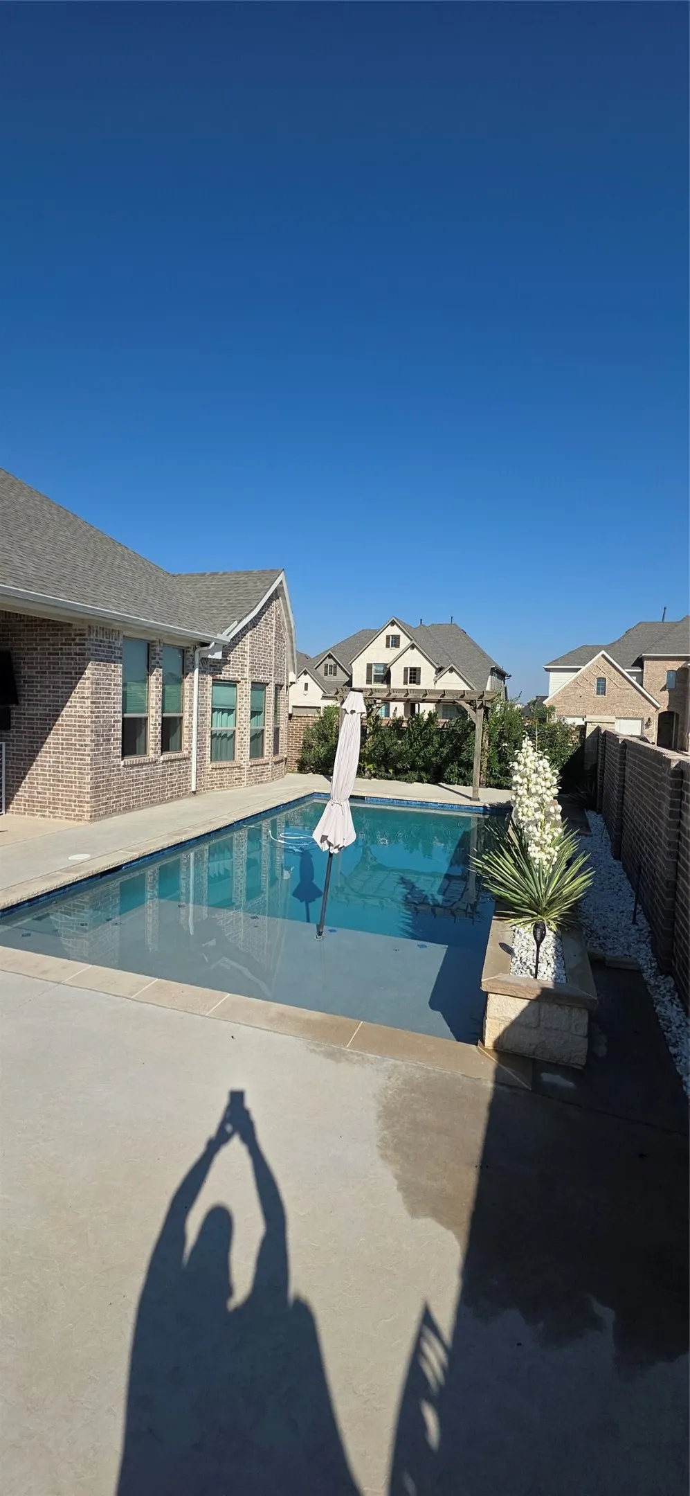 Concrete patio with a rectangular swimming pool, brick exterior, and a privacy fence