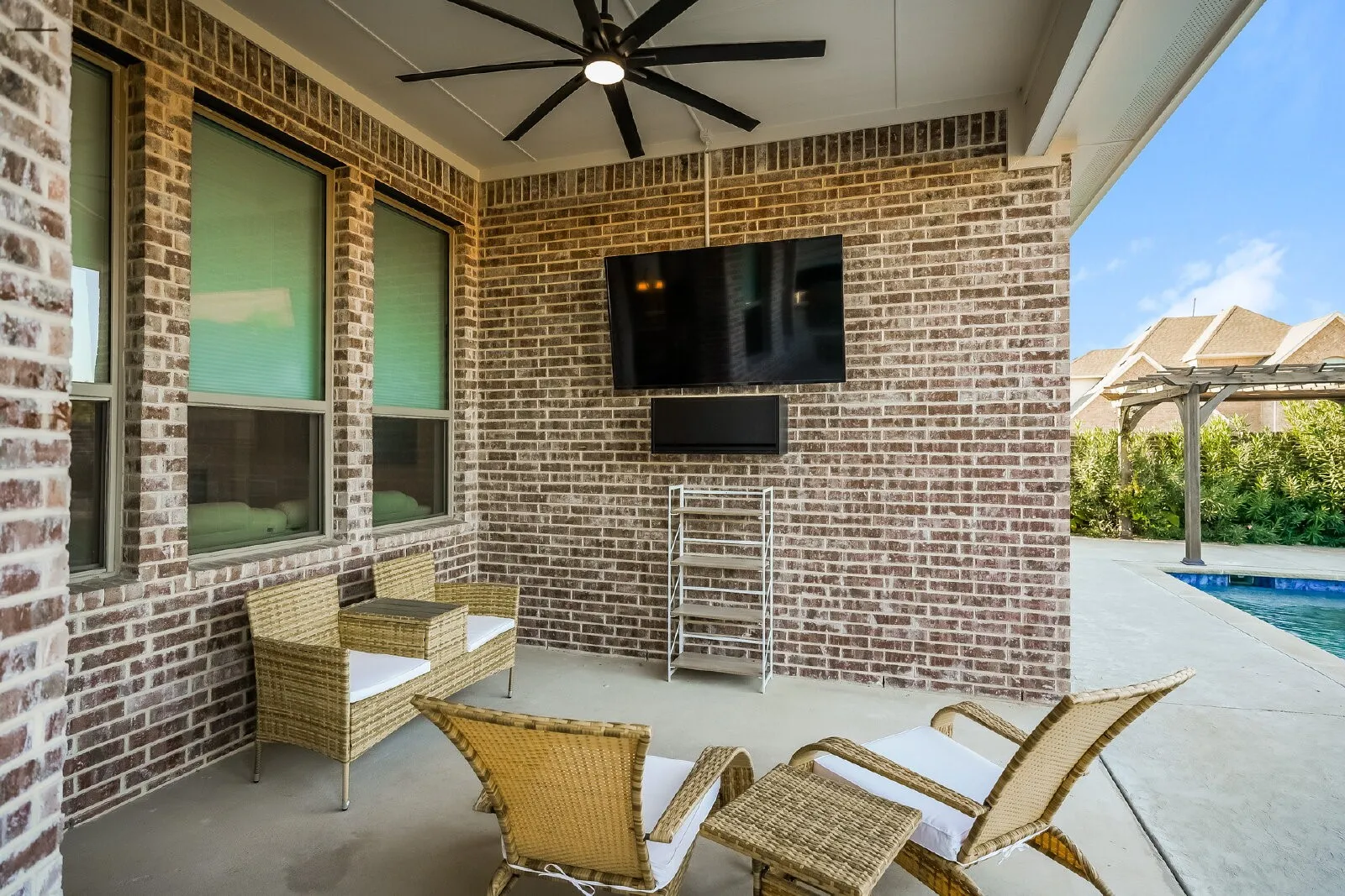 Covered patio featuring a ceiling fan, brick exterior, and a nearby swimming pool