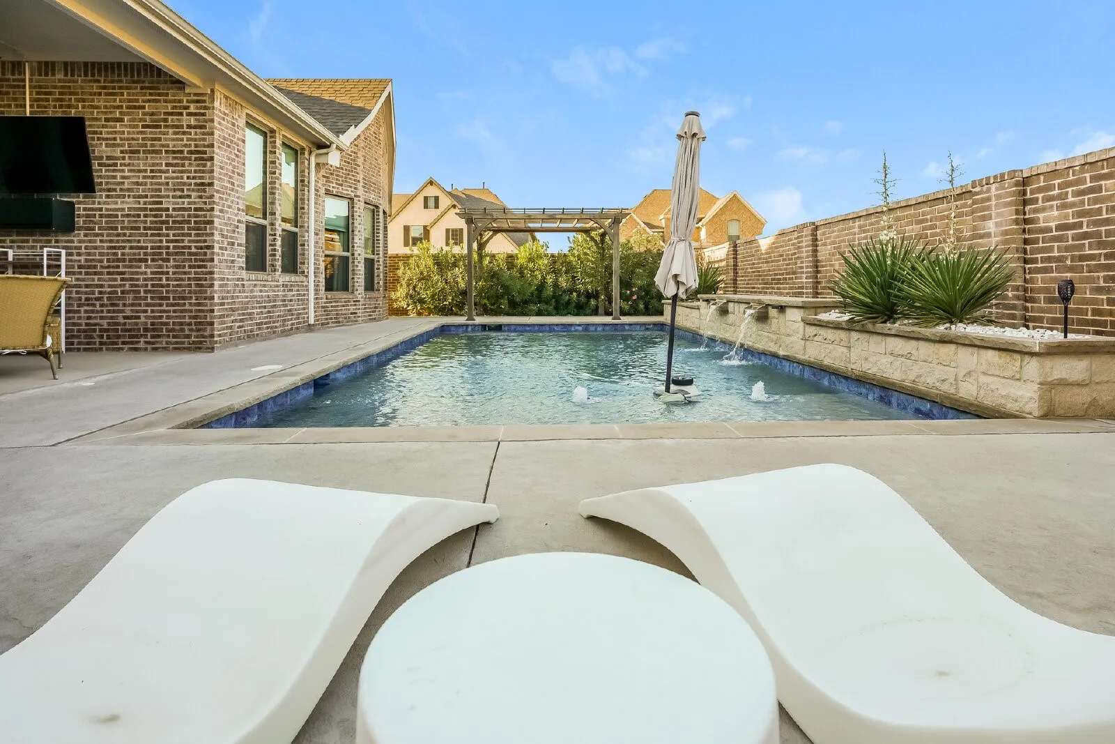 Spacious concrete patio with an in-ground pool featuring water fountains