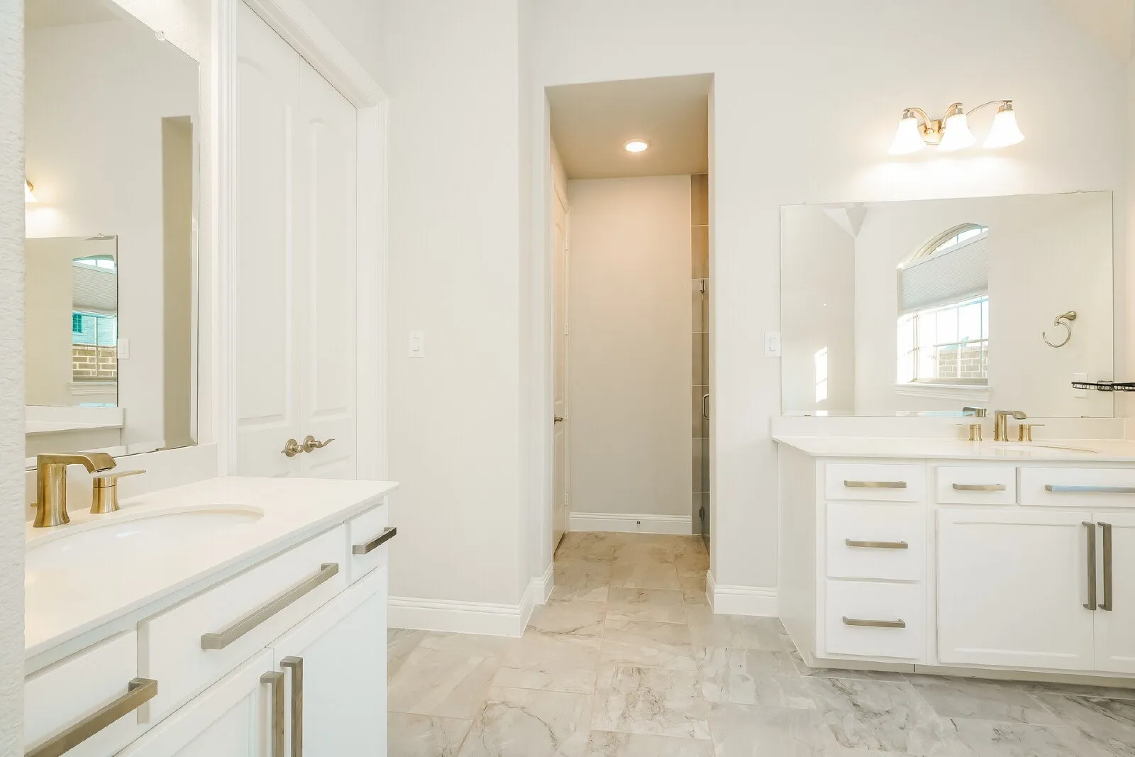 Dual vanity with white cabinetry, gold-finish fixtures, and a large wall-mounted mirror