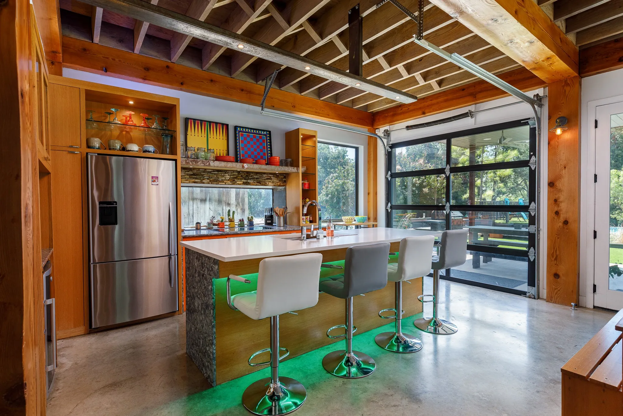 Exposed wood beam ceiling, concrete flooring, full-light roll-up door, stainless steel refrigerator, and built-in wood cabinetry