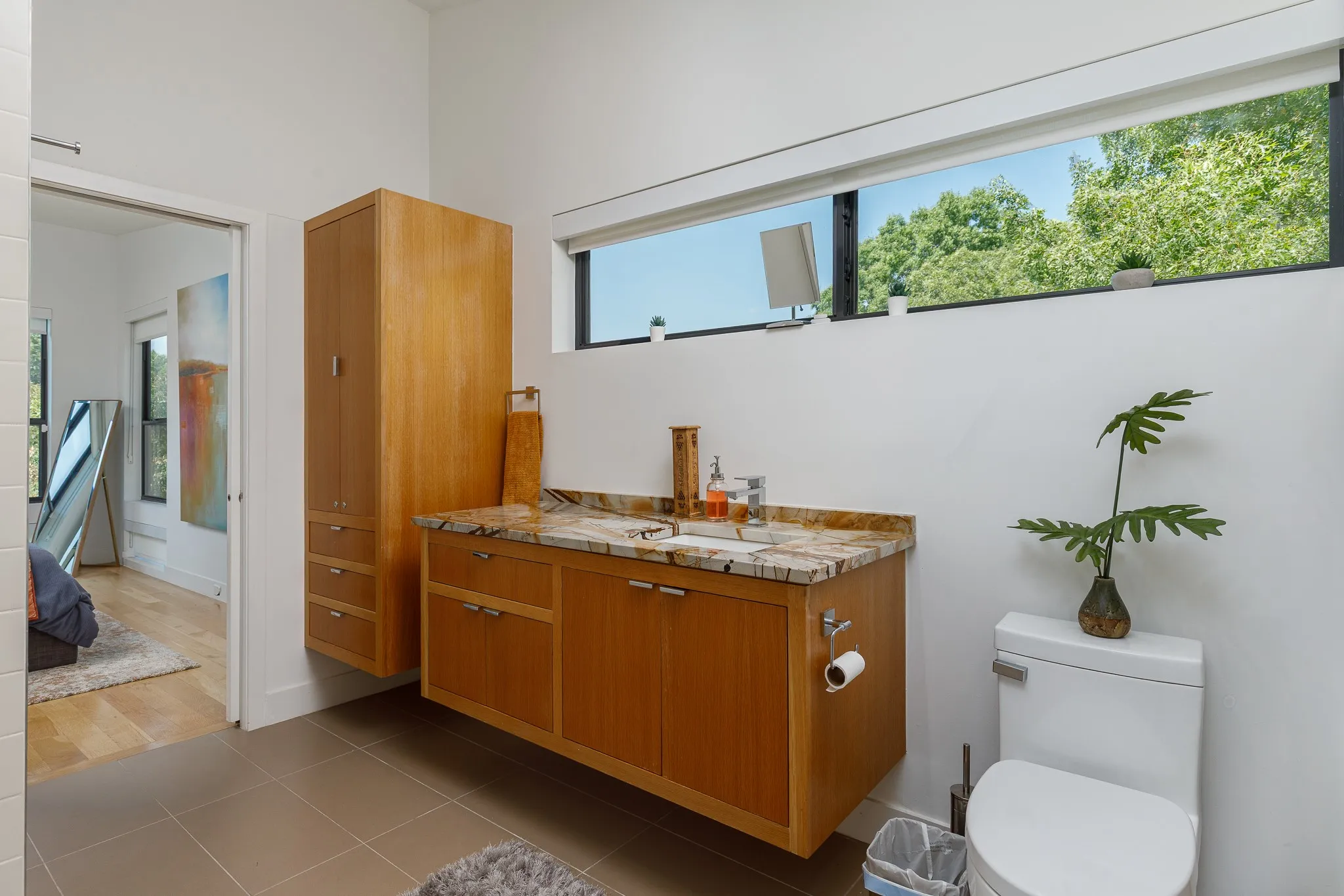Floating wood-finish vanity with a stone countertop, under-mount sink, and wall-mounted storage cabinet