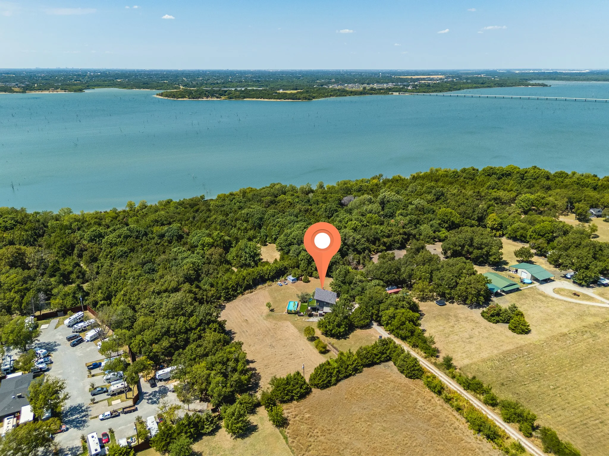 Expansive waterfront property with a residential structure, mature trees, and a paved road