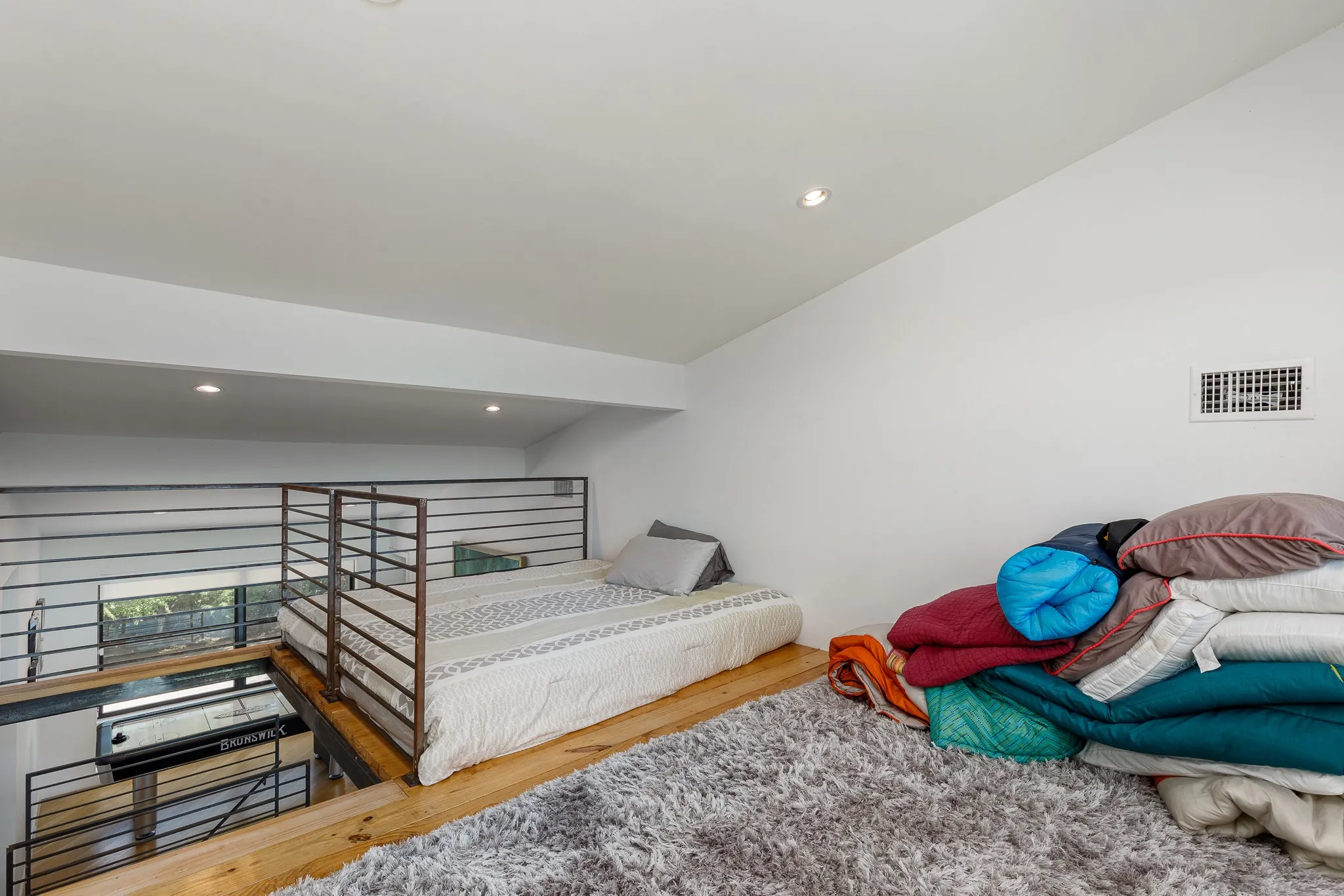 Upper level loft space with recessed lighting, exposed wood beams, and metal railing