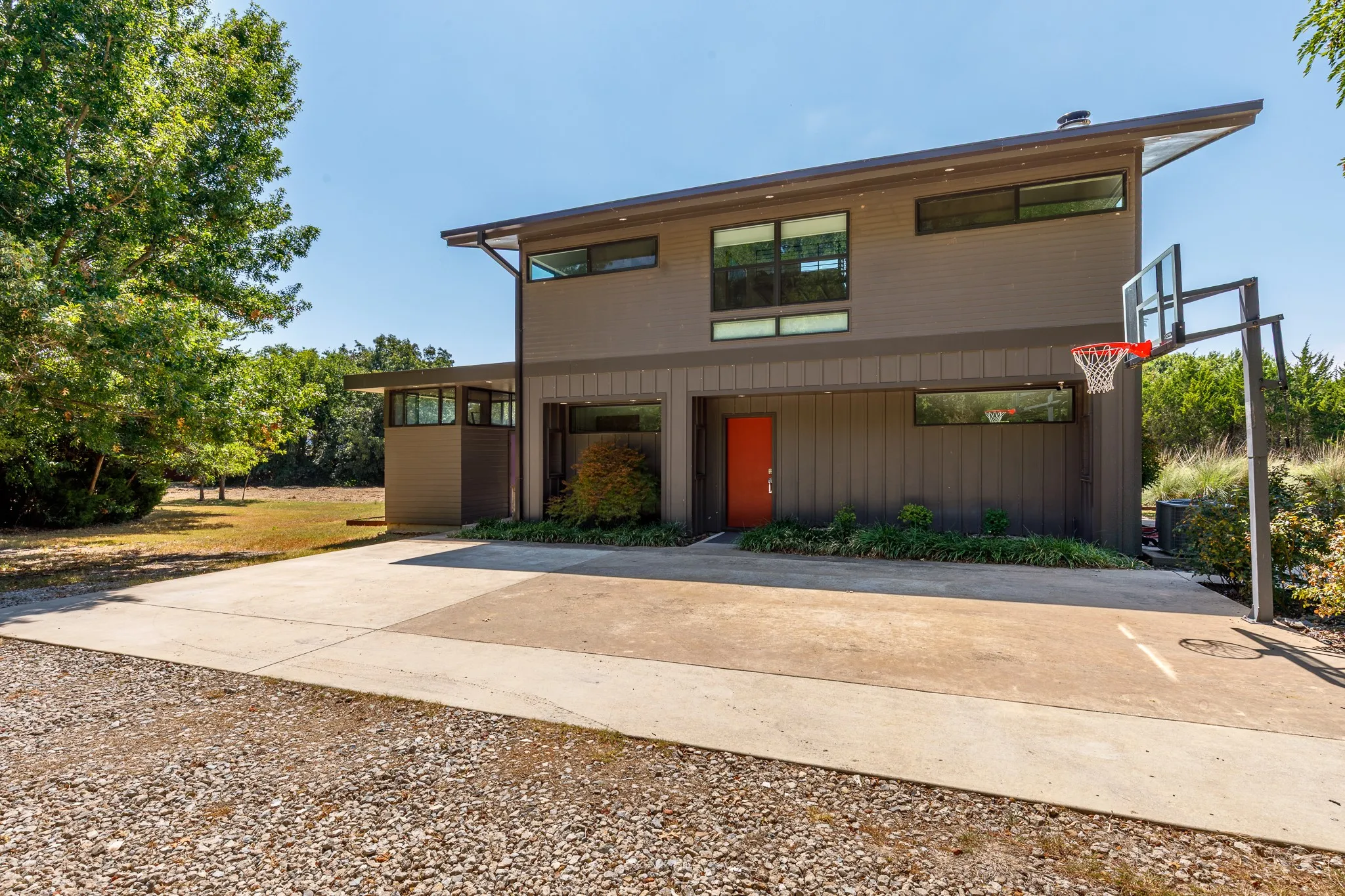 Modern two-story exterior with a sloped roofline, a vibrant red entry door, and bastball net on concrete path