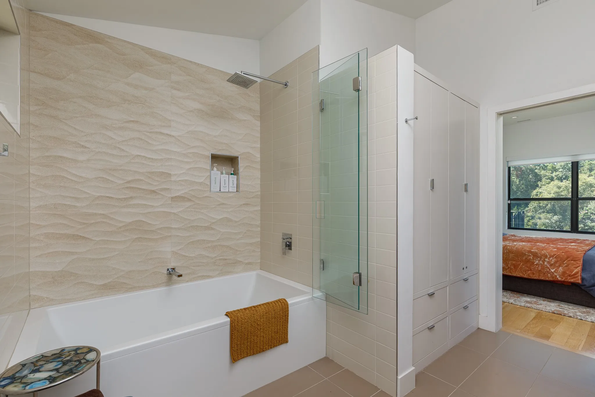 Bathtub with wall-mounted faucet and showerhead, glass shower partition, and built-in storage cabinetry
