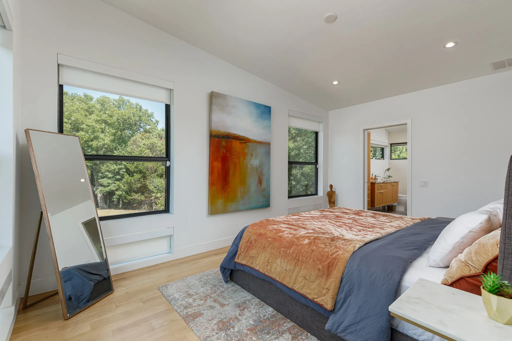 Recessed ceiling lighting, wood-finish flooring, two large windows, white walls, and a visible doorway leading to an additional space