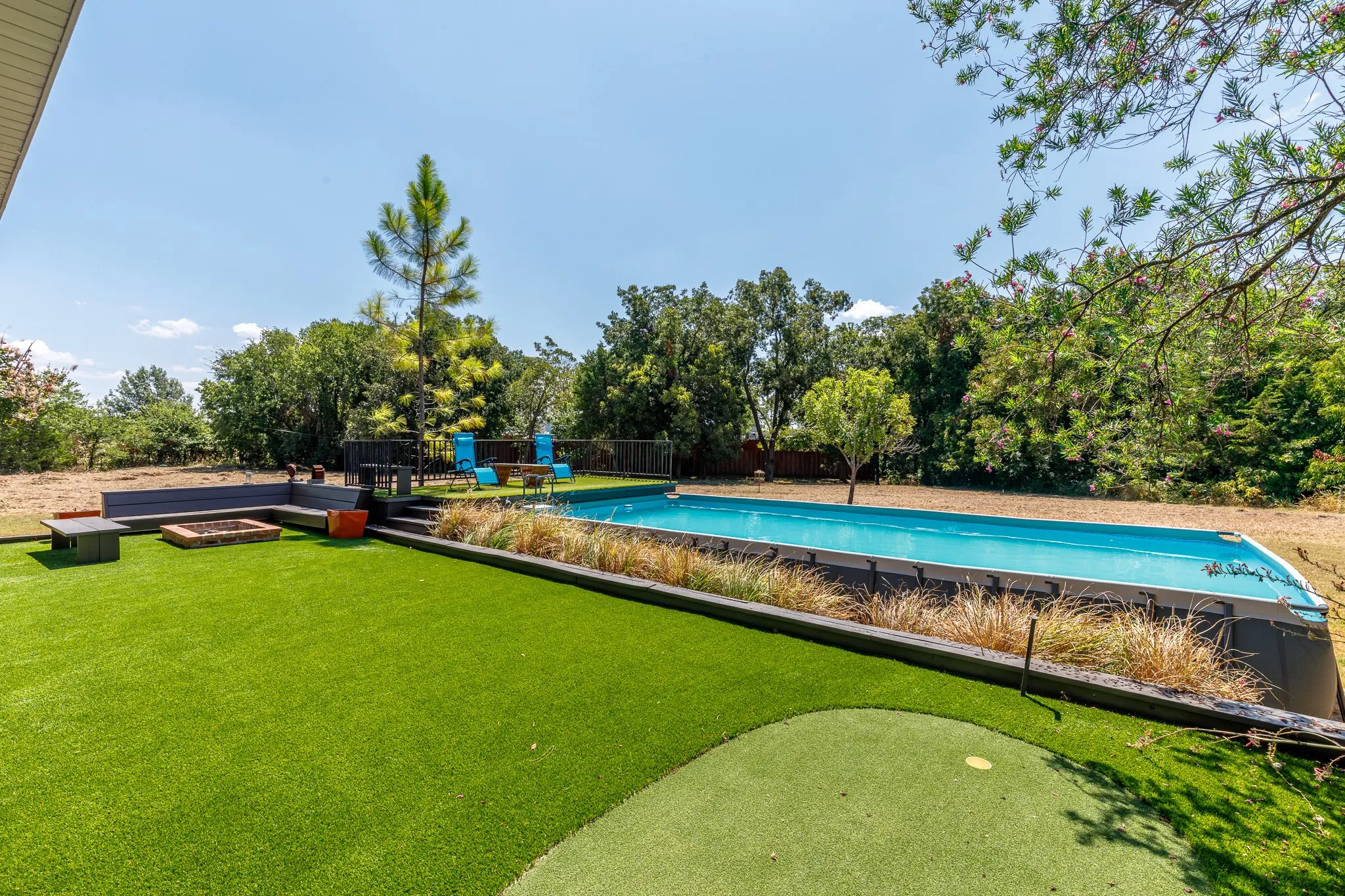 Backyard featuring an in-ground swimming pool, artificial turf, putting green, built-in wooden seating, a fire pit, and 1 of 5 puttin greens
