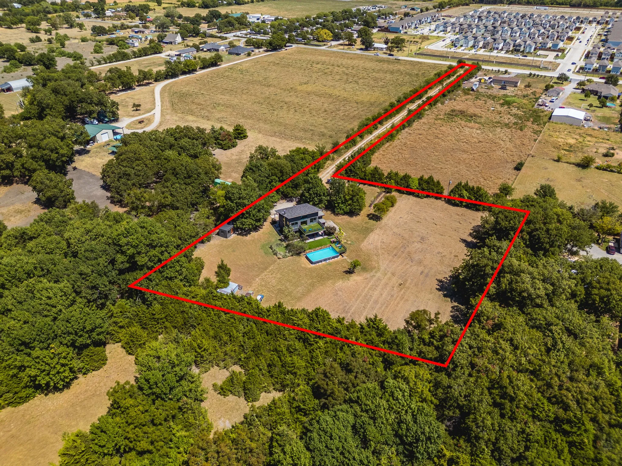 Expansive property featuring a modern residence, a rectangular swimming pool, and extensive tree coverage, with open land parcels
