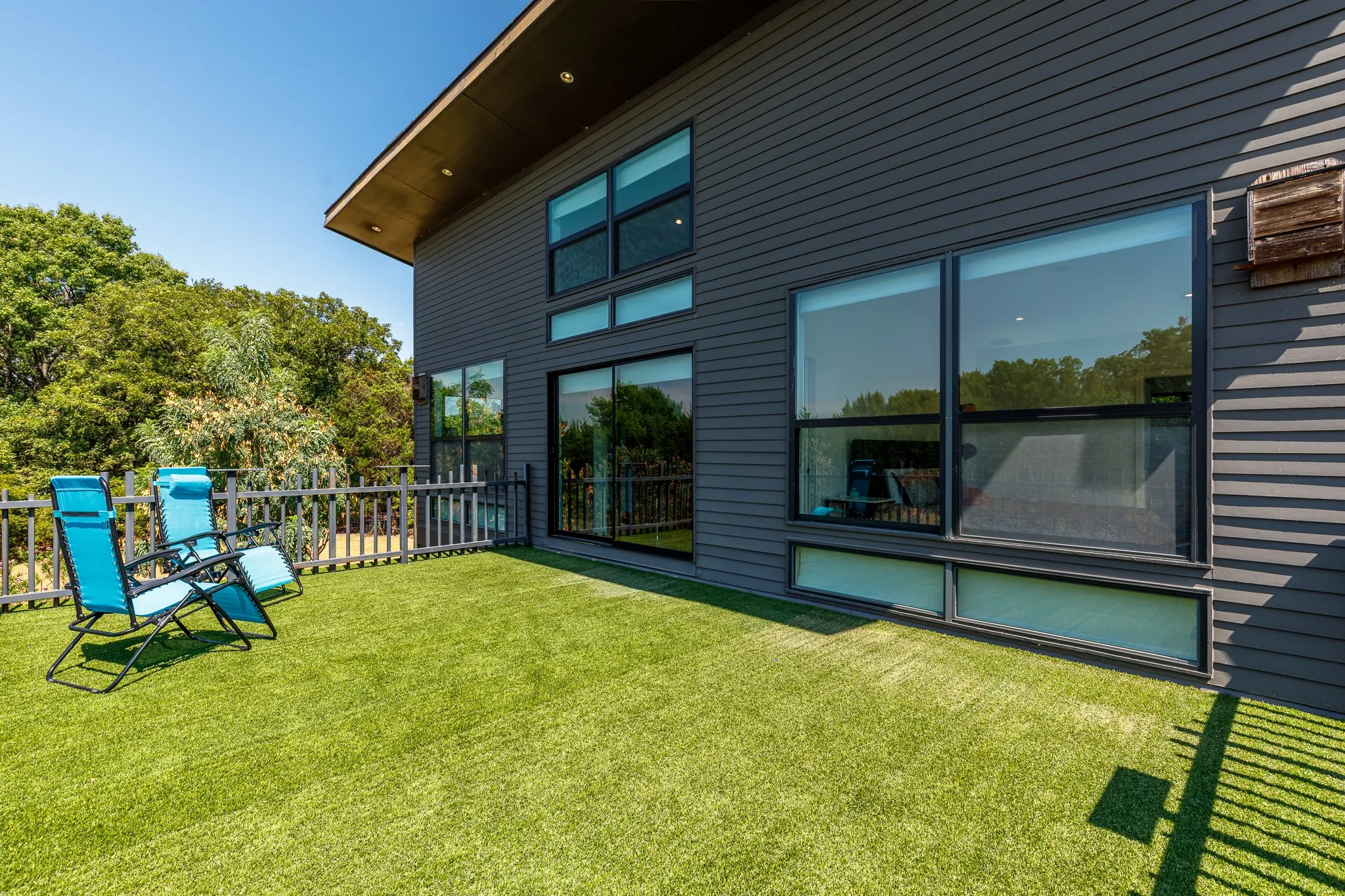 Expansive outdoor deck featuring artificial turf, a white picket fence, and dark siding