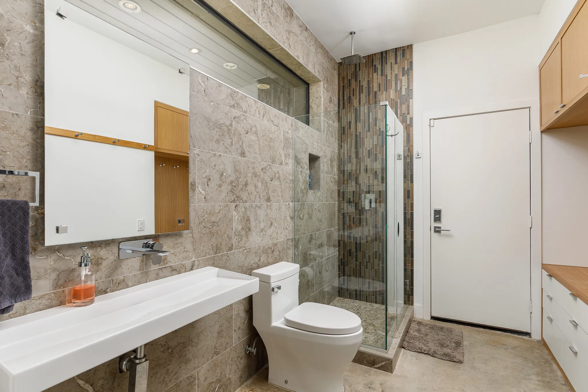 Wall-mounted rectangular sink, glass-enclosed shower, tiled shower surround, recessed shower niche, and custom wood cabinetry