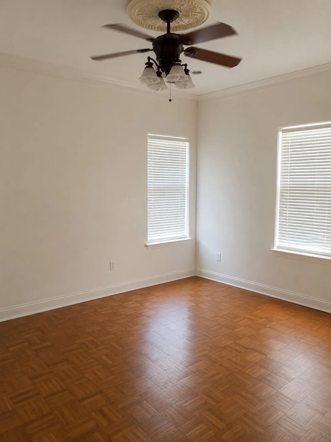 Recessed parquet wood-finish flooring, crown molding, ceiling fan with light fixture, decorative ceiling medallion, and multiple windows with blinds