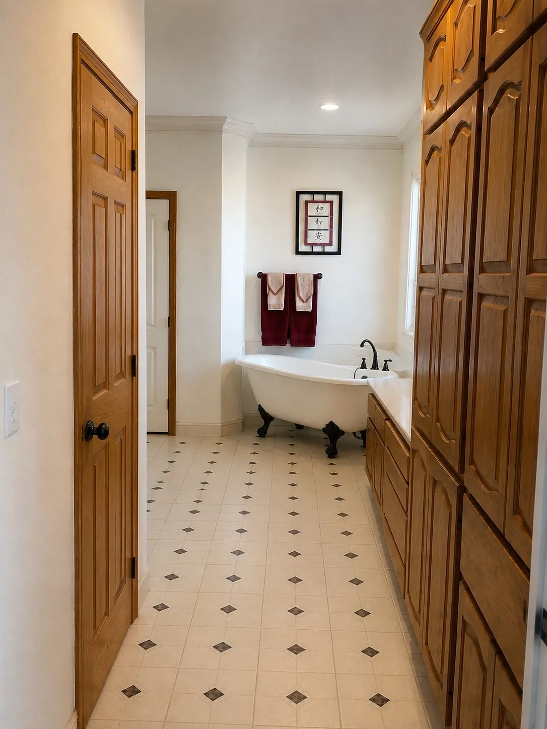 Freestanding clawfoot tub, extensive built-in wooden cabinetry, recessed lighting, crown molding, and tiled flooring with decorative inlays