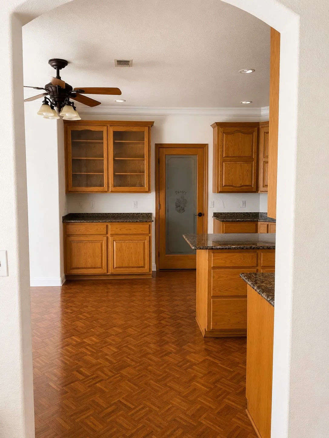 Parquet wood-finish flooring, recessed lighting, wood cabinetry with glass-front uppers, granite-style countertops, and a wood-paneled pantry door