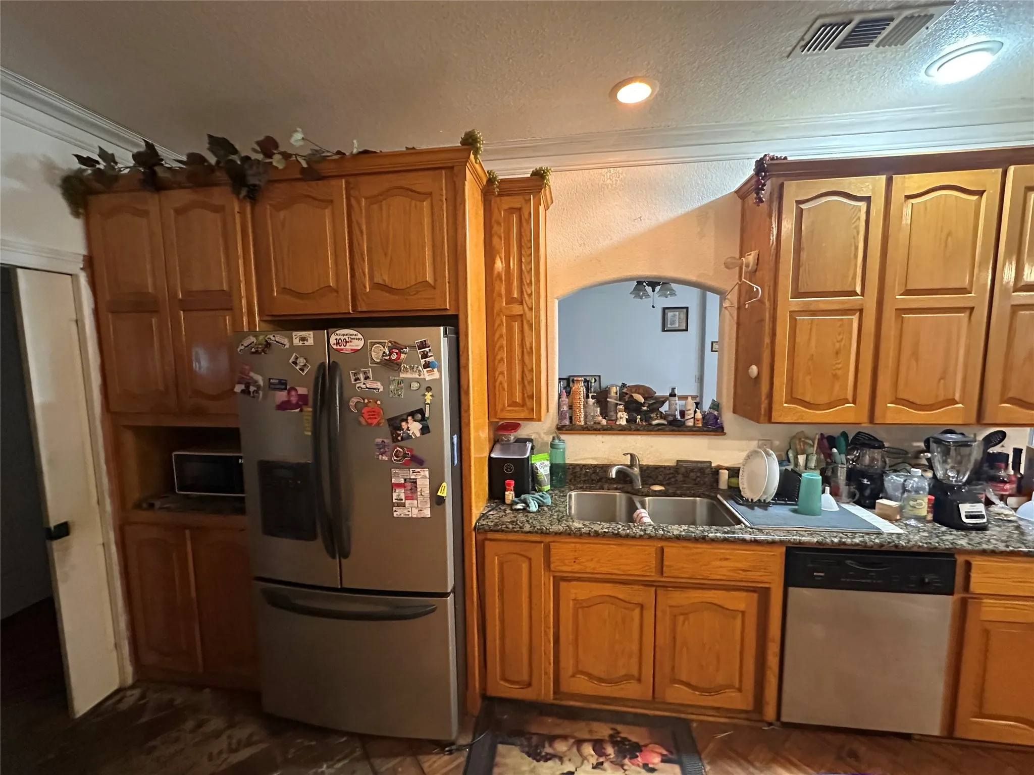 Full-height wood-finish cabinetry, recessed ceiling lighting, arched pass-through window, double basin sink, and stainless steel dishwasher