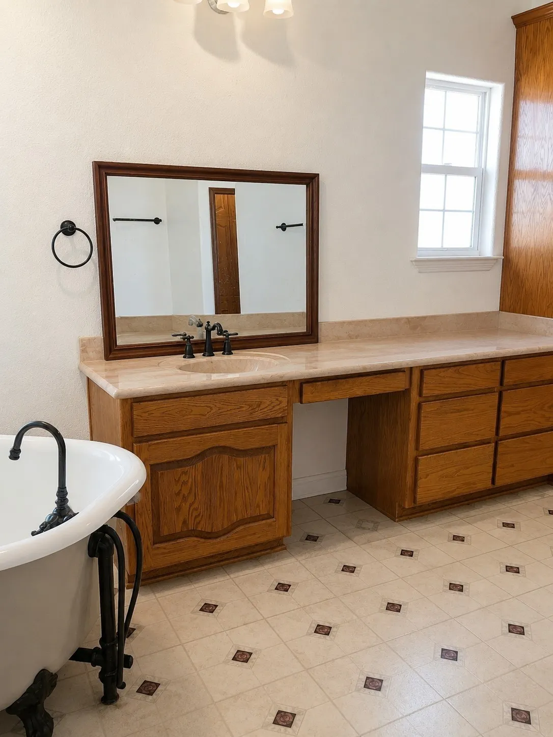 Freestanding clawfoot tub, wood vanity with integrated sink, stone countertop, framed mirror, and patterned tile flooring