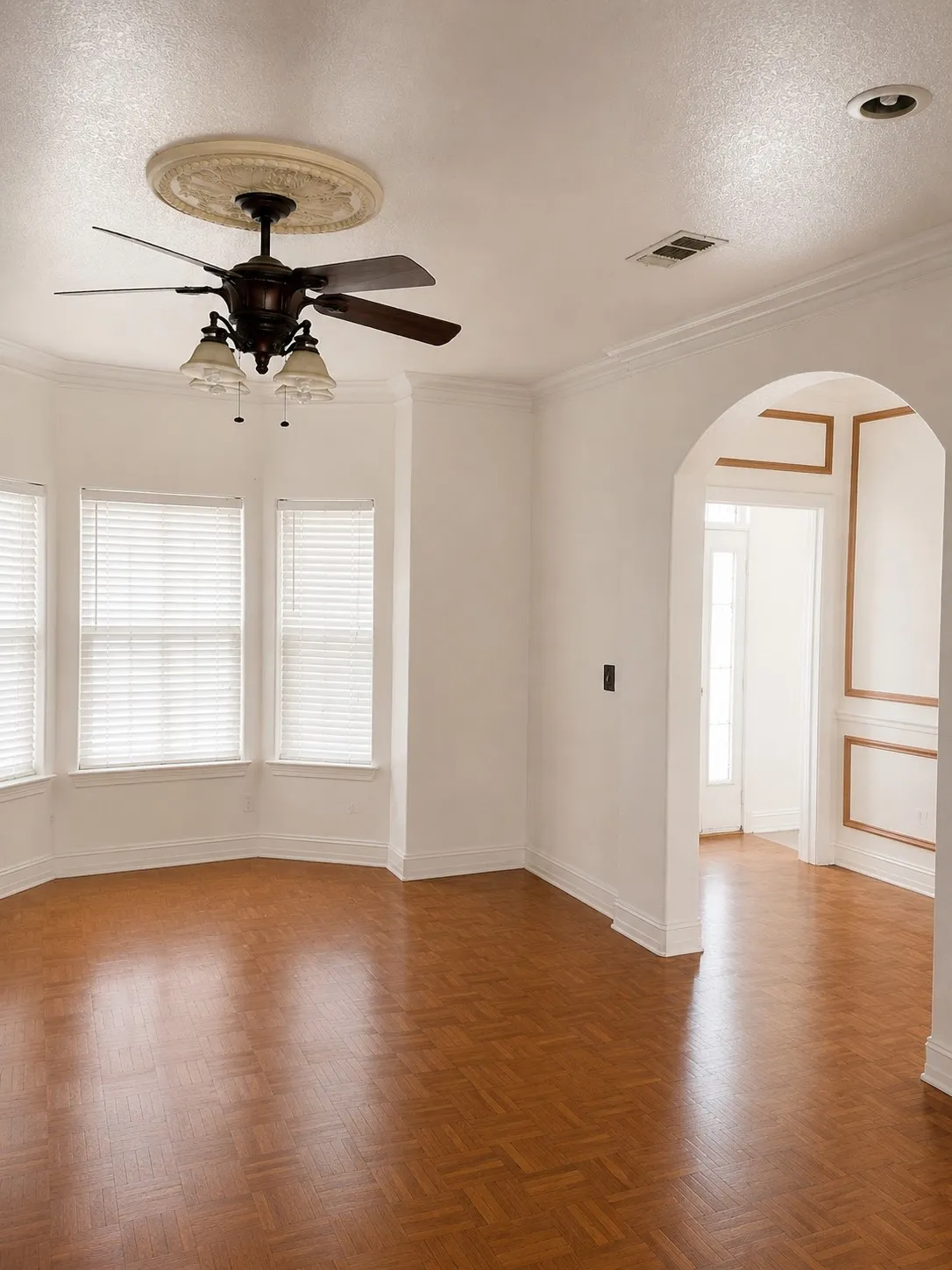 Bay window, parquet wood-finish flooring, ceiling fan with light fixture, crown molding, arched doorway