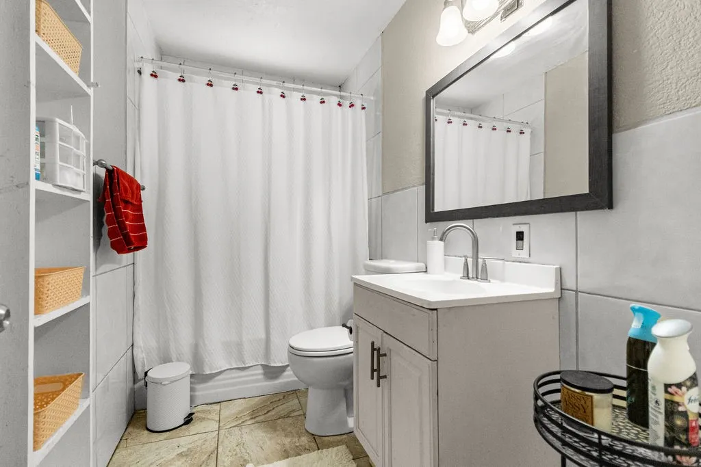 Bathroom featuring tile flooring, a single vanity with storage, built-in shelving, a framed mirror, and a shower with a shower curtain