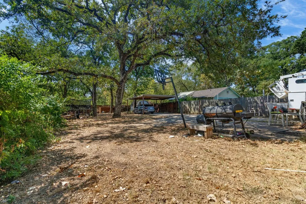 Expansive outdoor area featuring mature trees, a paved patio, and a covered carport