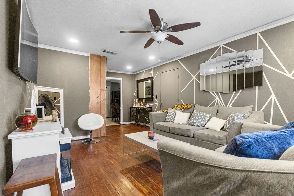 Wood-finish flooring, recessed ceiling lighting, ceiling fan, accent wall with geometric pattern, and a wooden sliding door