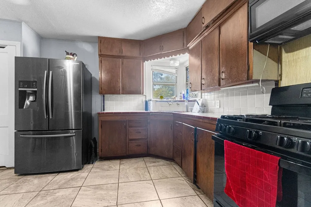 Kitchen featuring wood cabinetry, white tile backsplash, a stainless steel refrigerator, and a gas range