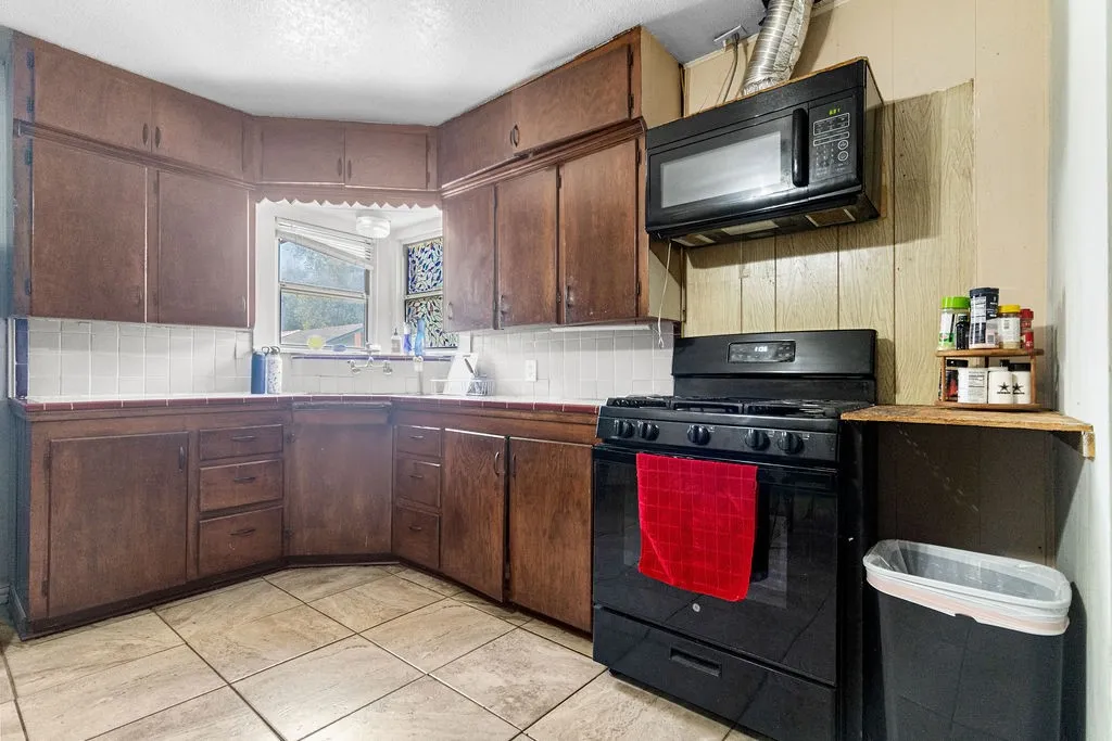 Kitchen featuring wood-finish cabinetry, tile flooring, tile countertops, a tile backsplash, and a built-in microwave
