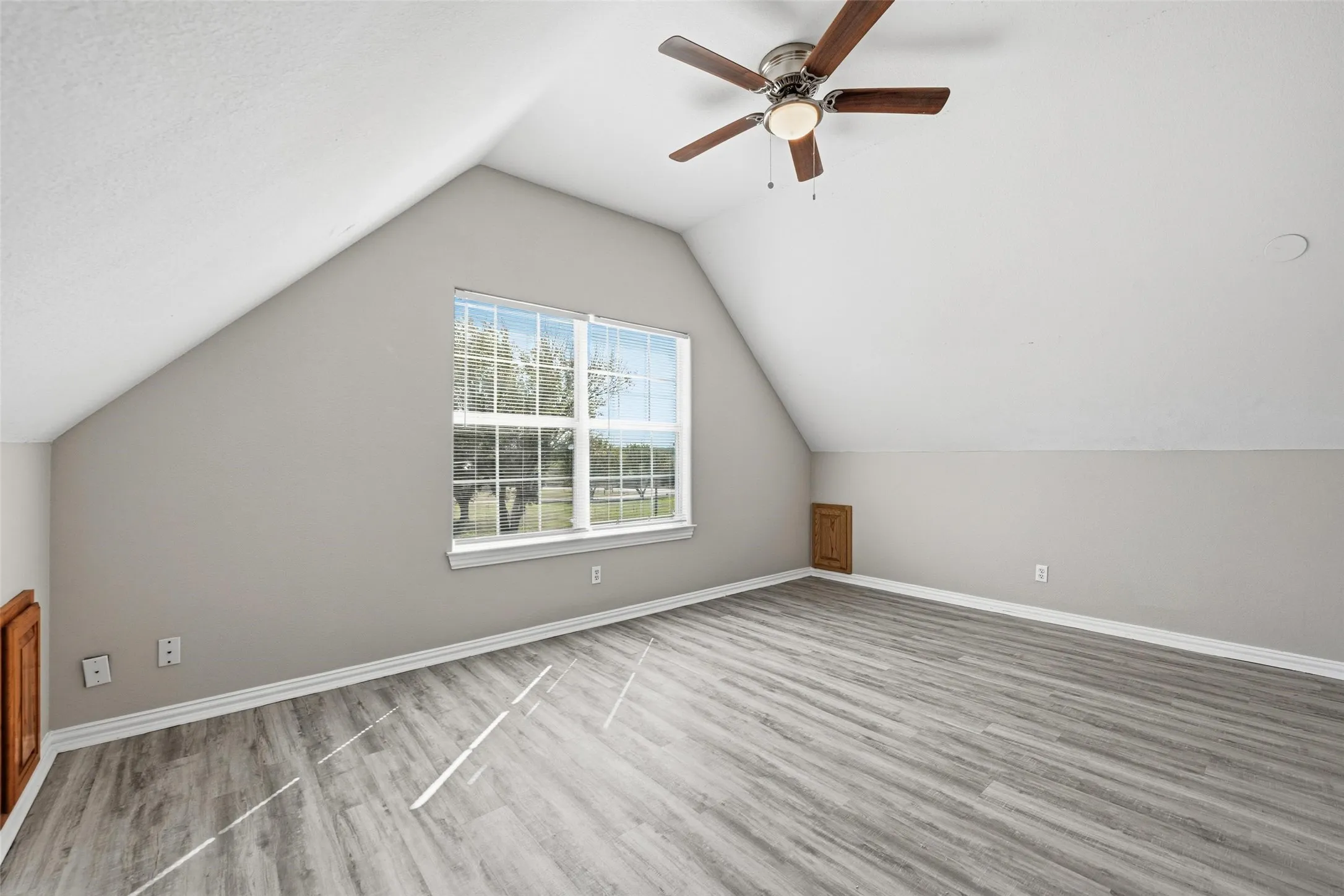 Vaulted ceiling with a ceiling fan, wood-finish flooring, and a window with white trim