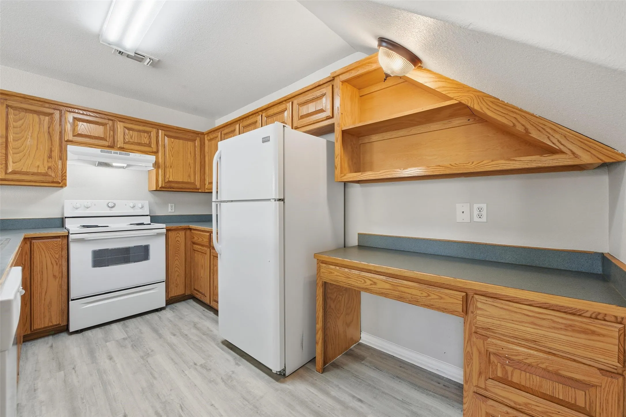 Wood-finish flooring with full kitchen cabinetry, white appliances, and built-in desk with shelving